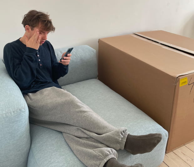 A picture of a man sitting on a couch looking at his phone while holding his head.