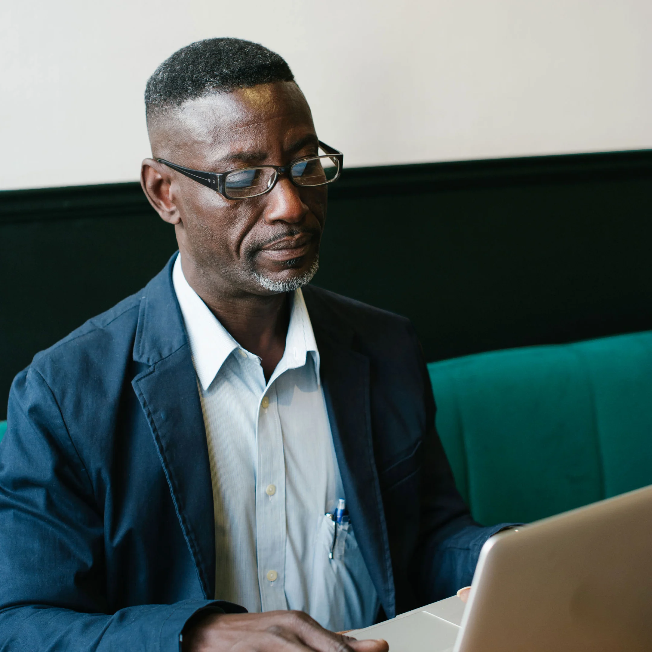 A man in casual business wear sits with his laptop on a green sofa