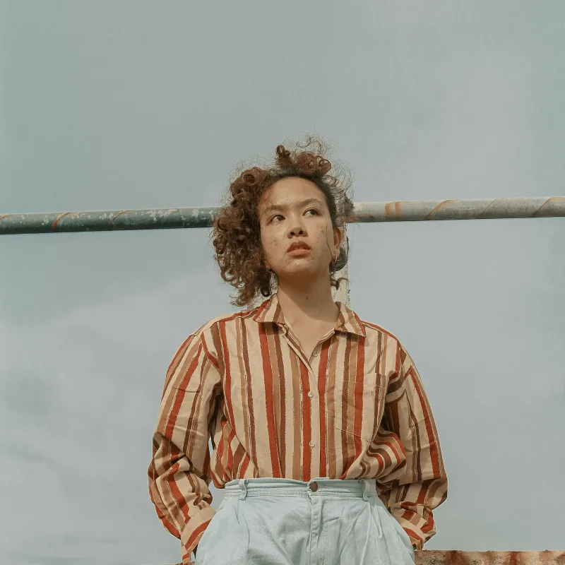 A woman in a striped brown and beige shirt looks up at the skies