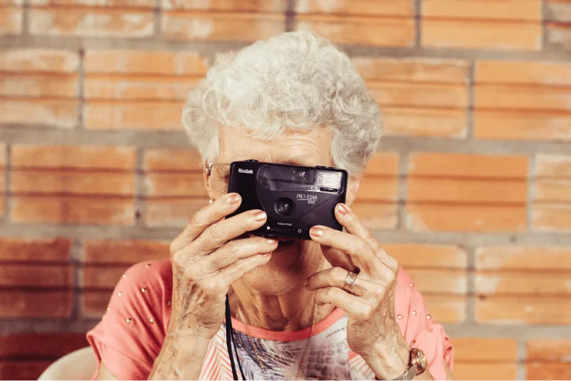 An elderly woman with white curly hair gets ready to take a photo with a camera